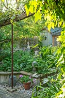 Small town garden in spring with ornamental garden shed, Grape vine trained on rustic reclaimed oak beam, Raised beds made from reclaimed bricks and stone. May