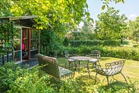 Table and chairs set out on lawn beside summer house  shaded by walnut tree. June