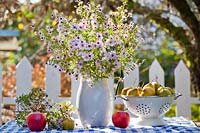 Jug of asters and harvested fruit on table, October.