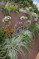 A wall of raised beds makes use of small spaces and is planted up with a mix of perennials such as Agapanthus 'Silver Moon', Geum 'Totally Tangerine' and Kniphofia 'Lemon Popsicle' in the Live Garden at Tatton RHS Flower Show 2017