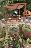 A corroded steel frame pergola with thermowood roof slats with Echinocactus grusonii growing in rusty oil-drums and other drought-tolerant cacti and perennials in the Cactus Direct:2101 Garden at Tatton RHS Flower Show 2017