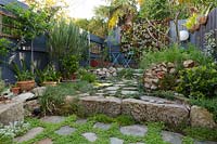 Wide view of inner city courtyard garden with greenwall of succulents, sandstone raised bed, flagged sandstone paving, and various plantings, November.
