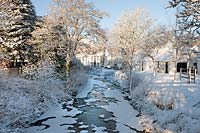 Snow covering the frozen Water of Gregg, trees and buildings, Barr Village, South Ayrshire, Scotland. January.