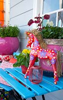Bright blue slatted table with pink pots and a red horse painted with a floral pattern, August.