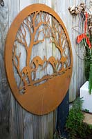Rusty metal wall plaque with a cut out kangarooss on timber paling fence, August.