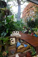 View from the covered entertaining area to a raised garden with timber decking. Eclectic collection of pots and garden ornaments featuring ceramic hearts and a rabbit ornament.