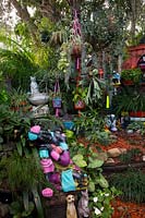 A Thai style resting Buddha statue painted black, pink, purple and blue in amongst shade loving plants and other garden ornaments.
