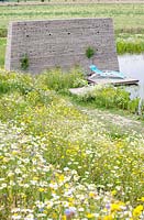 Surrounded with wildflowers swimming pond with tower made of recycled paving tiles near a concrete jetty.