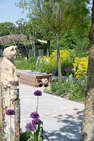 A cat carved from a birch stump next to alliums in the recycle garden