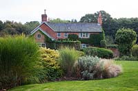 View of the house with island beds planted with shrubs and grasses including, Miscanthus, Euonymus and Stipa tenuissima.