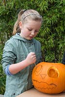 A young girl cuts out the outline of the second eye on a large pumpkin