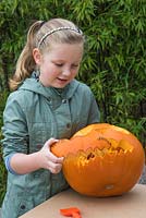 A young girl removes the outline of the mouth on a large pumpkin