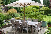 A sheltered dining terrace, separated from the lawn by pots of leafy sumach.