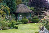 Thatched summerhouse with box topiary domes in autumn garden, September.