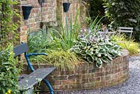 A half moon raised brick bed planted with Hosta and ornamental grasses.