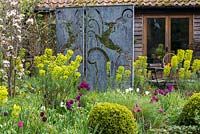 Metal screen by Paul Richardson creates privacy for sheltered patio,  borders of tulips and Mediterranean spurge.