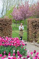 Philippa Burrough looks over the gate leading to a meadow. Behind, cherry trees in blossom.