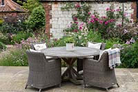An outdoor dining area beside a bed of Roses, Thalictrum, Cistus and Scabious.