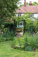 In a long town garden, a rose arch leads from a middle area of flower borders, to a gravel courtyard beside the house.