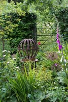 A round metal globe is perched on a chimney pot in a summer border