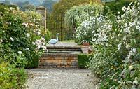 Gravel path, raised pool, gate and heron bird sculpture by Michael Lythgoe - Bourton House Garden, Gloucestershire
