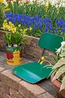 A tin can planted with flowering Hyacinthus is displayed on a stone wall next to a reused green seat at Keukenhof Gardens, The Netherlands.  
