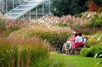Grass borders and visitors on bench by 'Princess of Wales' conservatory - Royal Botanic Gardens, Kew