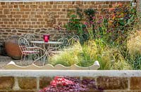 Small courtyard garden with table and chairs, Stipa tenuissima, Cirsium rivulare 'Atropurpureum', Cercis canadensis 'Ruby falls'