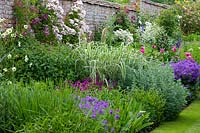 Walled garden with herbaceous border in summer, border contains Peonies, Tradescantia, Clematis, Roses and hardy Geraniums