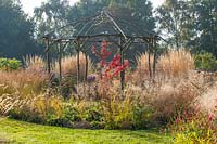 Rustic gazebo of coppiced ash and hazel surrounded by grasses such as Calamagrostis x acutiflora 'Karl Foerster'