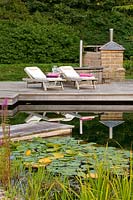 Decking beside 'natural' swimming pool with sun loungers and outdoor oven and barbecue
