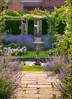 View through rose garden with beds edged with Nepeta faassenii - catmint to pond with statue to arches
