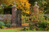 Iron gates in the formal walled garden with autumnal colour from borders and trees

 