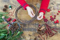 Using a piece of wire to attach small glass jars to natural wreath base