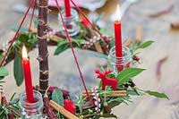 Close up detail of red themed advent candle holder with lit candles as centrepiece in a table setting