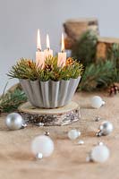 Festive candle holder made from cooking mould filled with pine foliage and cones in festive table setting with decorations
