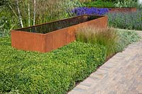 Contemporary garden with rusted corten steel water trough and green foliage planting. RHS Hampton Court Flower Show