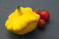 A yellow summer patty pan squash and cherry tomatoes on a stone slate background