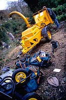 Large petrol engined garden chipper being used to clear overgrown garden Range of tools including wheelbarrow chainsaw