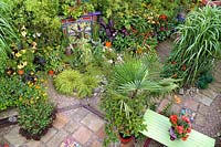 Colourful suburban back garden with architectural plants, mosaic paving, ornamental grasses and reclaimed fireplace feature