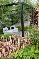 The Naturally Fashionable Garden designed by NDG+. Seating area with metal mesh seats, black pergola, birch logs & birch trees