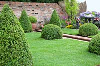 Garden scenery with ornamental shrubs, perennials and bux topiaries, iron garden furniture in the back ground