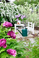 View into the garden with garden furniture, garden tools, watering can and bouquet of lilac