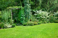 Garden scene with iron pergola, various shrubs, perennials, conifers and lawn