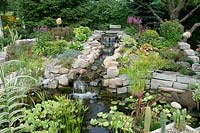 Pond with aquatic plants and waterfall, perennials and shrubs
