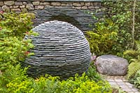 The Chelsea Flower Show 2005, London, UK. 'The Philosophical Garden' ( Andy Loudon ) stone sphere with negative image of itself in drystone wall behind. Spring time woodland planting