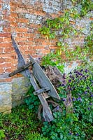Cerney House Gardens, Gloucestershire, UK. ( Sir Michael and Lady Angus ) Walled kitchen garden, ancient wooden wheelbarrow leaning against wall