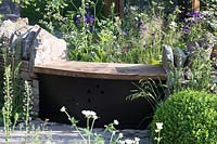 RHS Chelsea Flower Show 2014. 'Vital Earth The Night Sky Garden', designers David and Harry Rich. Simple wooden bench set into rustic wall.  
