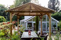 Jackie Healy's garden near Chepstow. Early autumn garden. Japanese style wooden 'pergola' shades dining table in the patio area