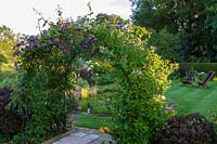 Sue O'Neill's garden at Field Cottage, Cirencester, Glos. Clematis and Honeysuckle arch lead through to lawned garden
